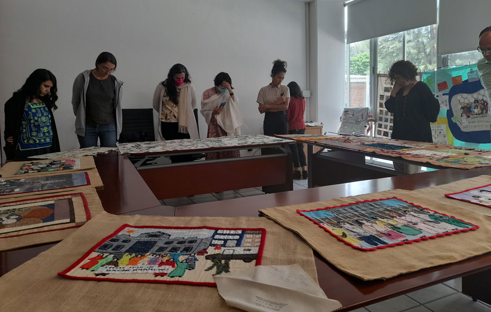 Attendees engaging with the textiles at day 2 of the 'Narrativas textiles. Tramas de dolor y empatía en América Latina' seminar. Some Conflict Textiles pieces are visible in the foreground. (Photo: Natalia Quiceno Toro)