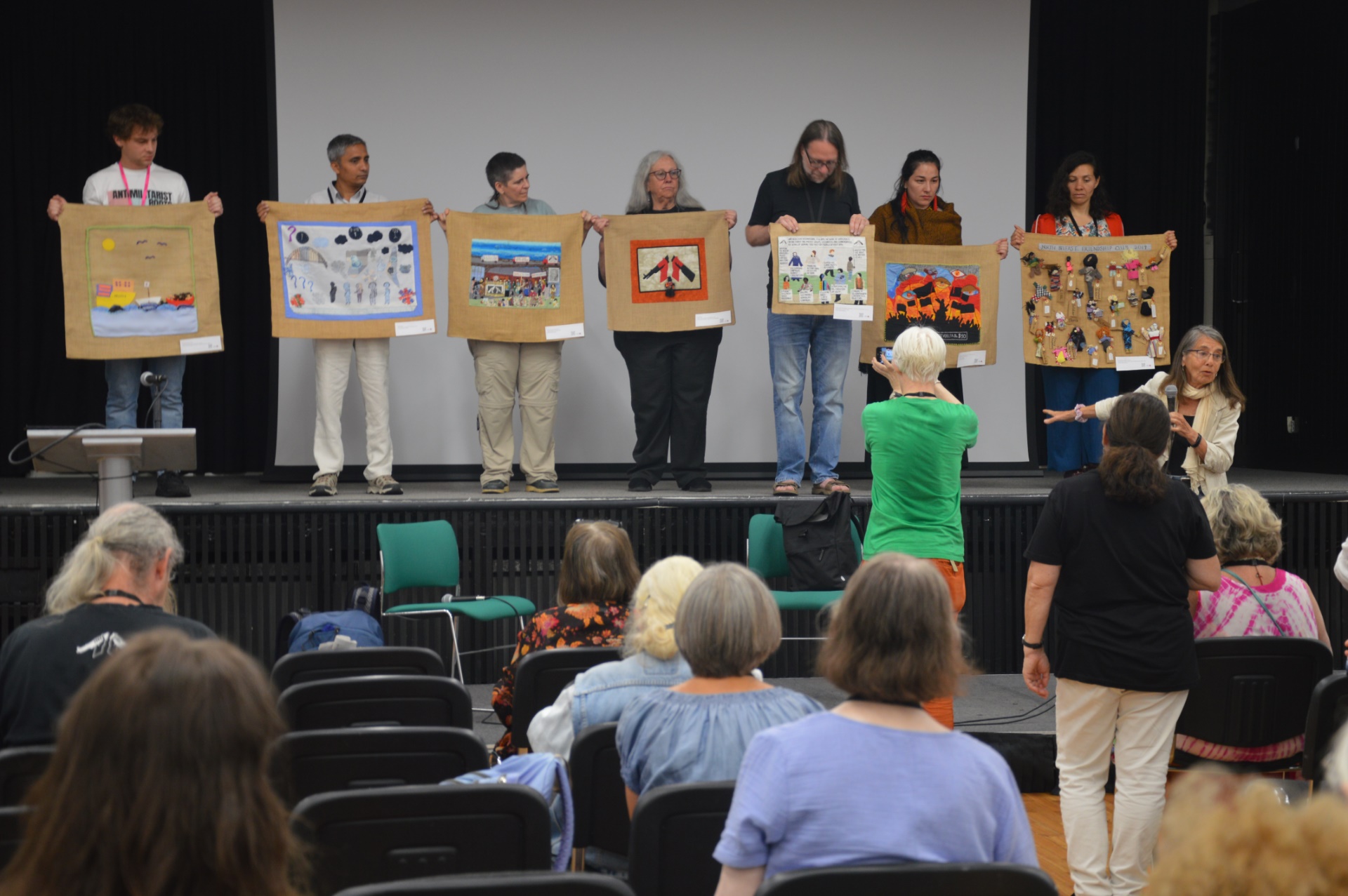 Conflict Textiles curator Roberta Bacic (right) at the WRI ‘Antimilitarist Roots’ conference (18 June 2023) engaging with participants in creating a 'Human Wall Of Resistance' using textiles from Conflict Textiles collection. (Photo: Jan Van Criekinge)